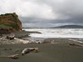 Grey sand beach with stones and driftwood with rough seas and grey sky in the background