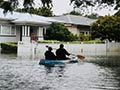 Two people travel down a flooded suburban street in a kayak.