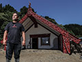 A man stands on a large pile of silt in front of a wharenui. 