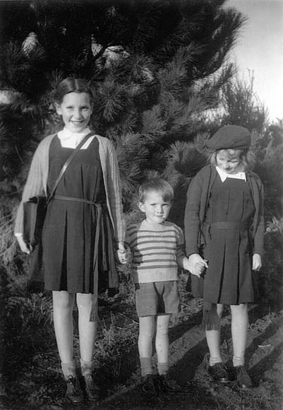 Two older girls posing each side of of boy standing in a garden