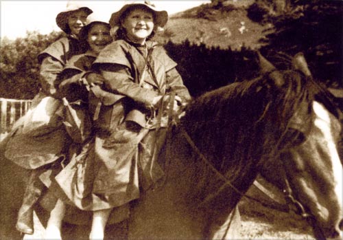 Three kids in oilskin coats on horseback