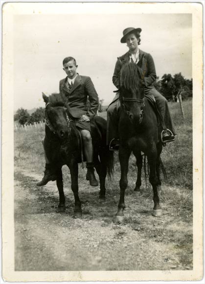 Boy and older girl sitting on horse back on farm track