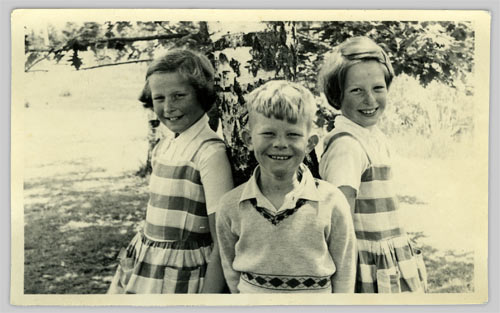 Boy with a girl on each side leaning against a tree