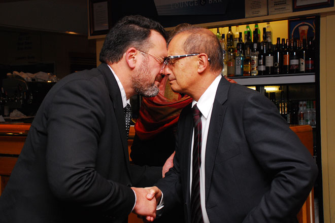 Two men in suits shaking hands and pressing their noses and foreheads together