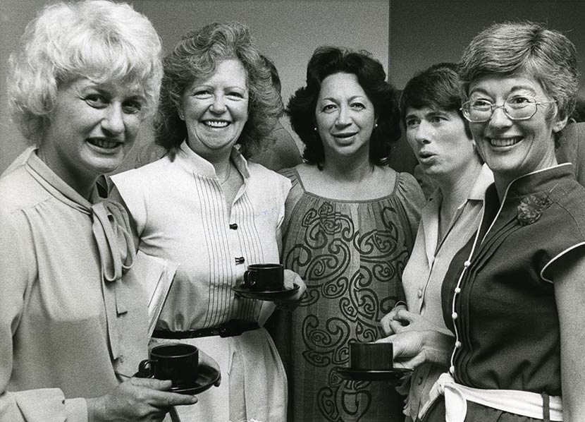 Five smiling women grouped together looking at camera