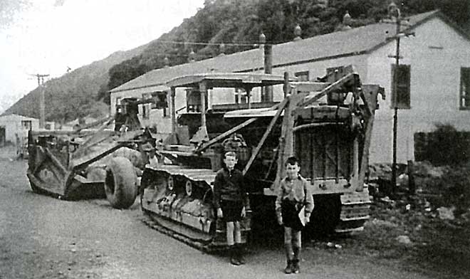 Two boys next to a large bulldozer in a railway yard