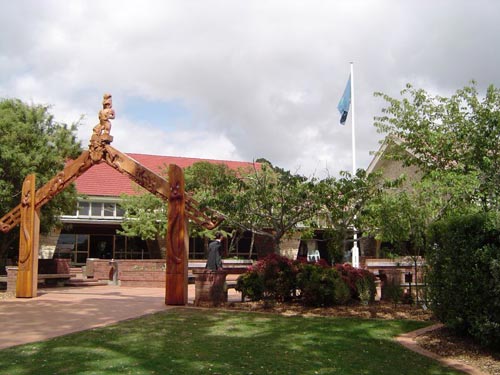A waharoa (Māori carved gateway) in front of buildings and adjacent to a flagpole.
