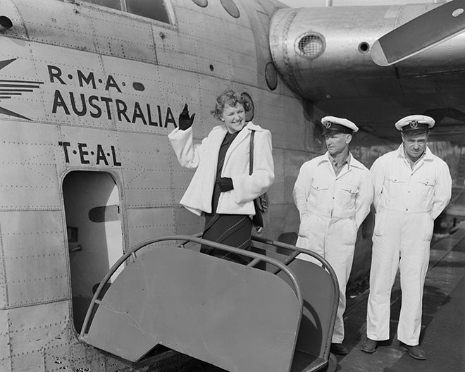 Woman waves as she boards a plane, two crew look on