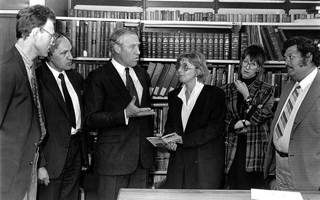Group of four men and two women in formal clothes gathered in library
