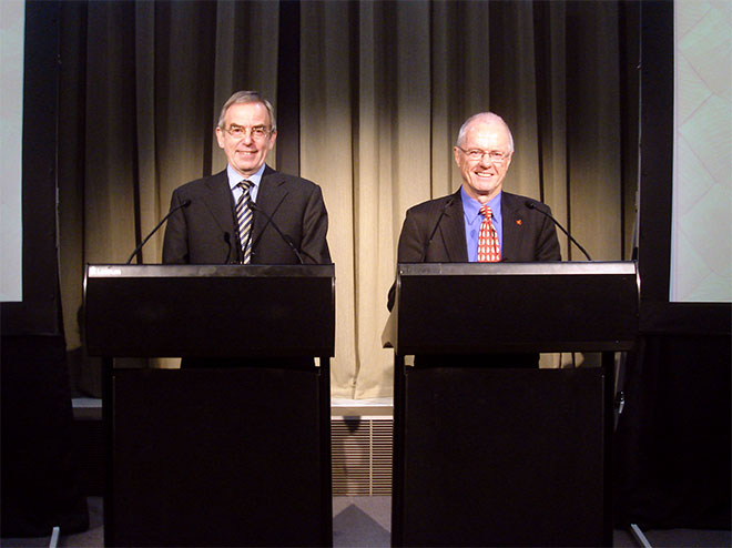 Two men standing at lecterns on stage