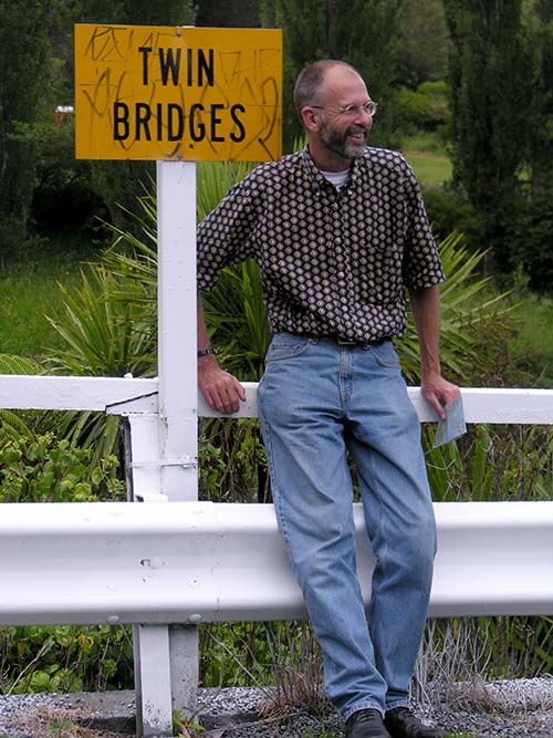 Man standing next to sign that says 'Twin Bridges'