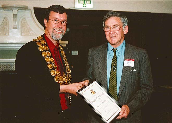 Man inmayoral chains awarding framed certificate to another man