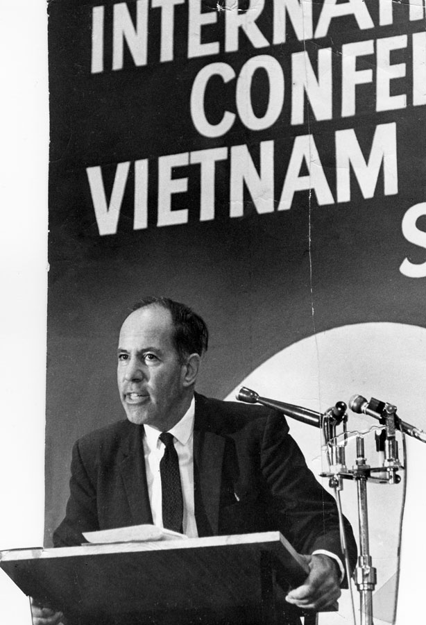 A standing man speaks from a podium, beneath a poster bearing the words ‘International Conference Vietnam.’ 
