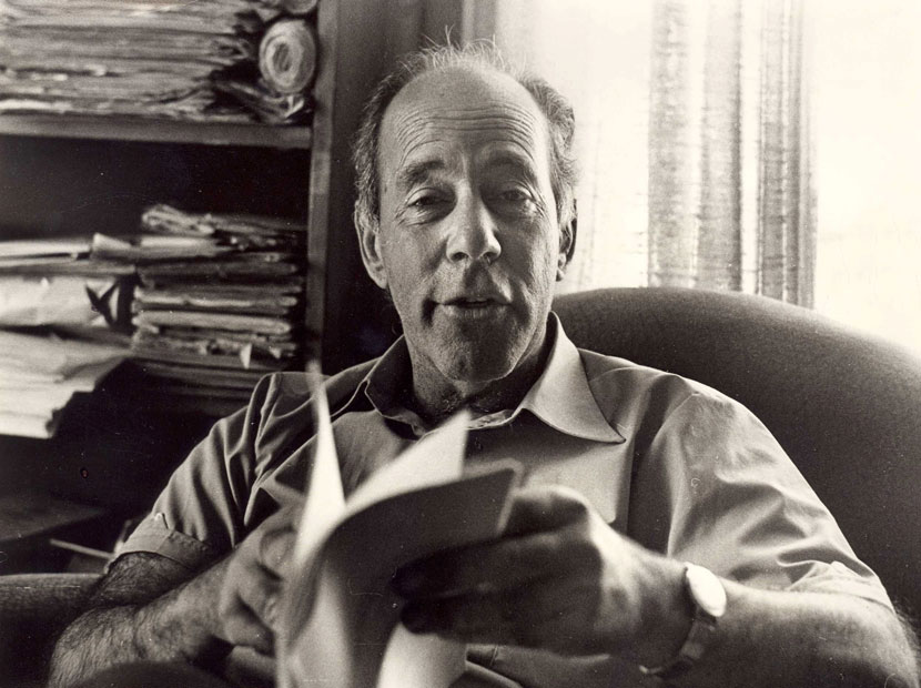 A seated man holding a booklet.