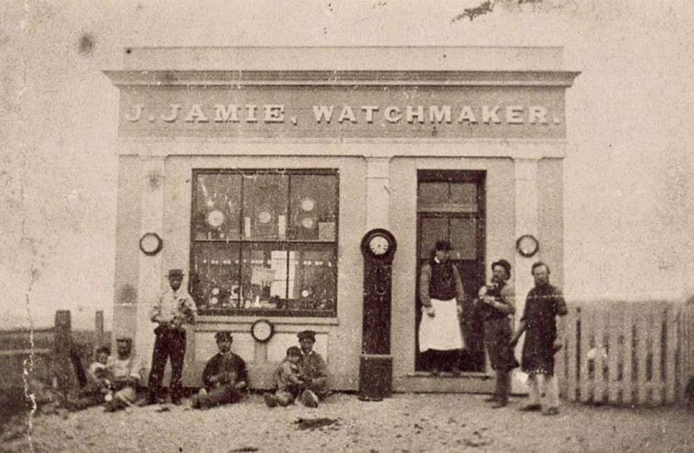 People sitting and standing outside a building named J. Jamie Watchmaker