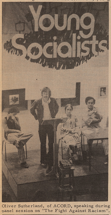 News Paper article showing people on stage with Young Socialists on banner behind