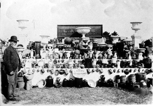 Luke Adams with examples of his firm's pottery at a show, 1897