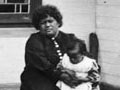 Kiti Karaka Rīwai (seated with child, right) in front of the meeting house she helped build at Wairua, Chatham Island, in the 1890s
