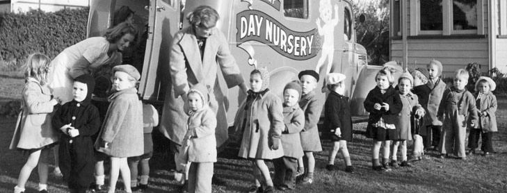 Kids and teachers outside building with 'Day Nursery' on wall