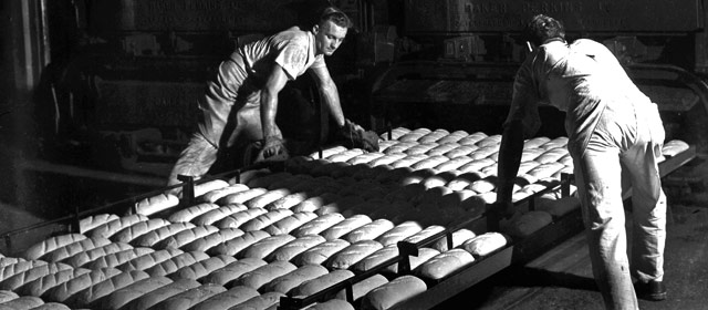 Workers lift trays of bread in a bakery