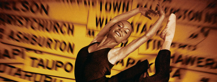 Ballerina in a dancing pose in front of collage of NZ town signs