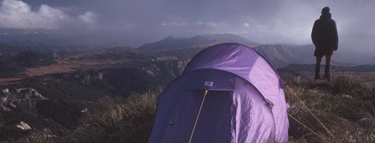 Man in front of tent looking over rugged hills