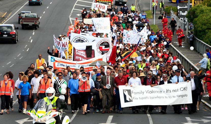 People marching along road holding signs, banners, and flags.