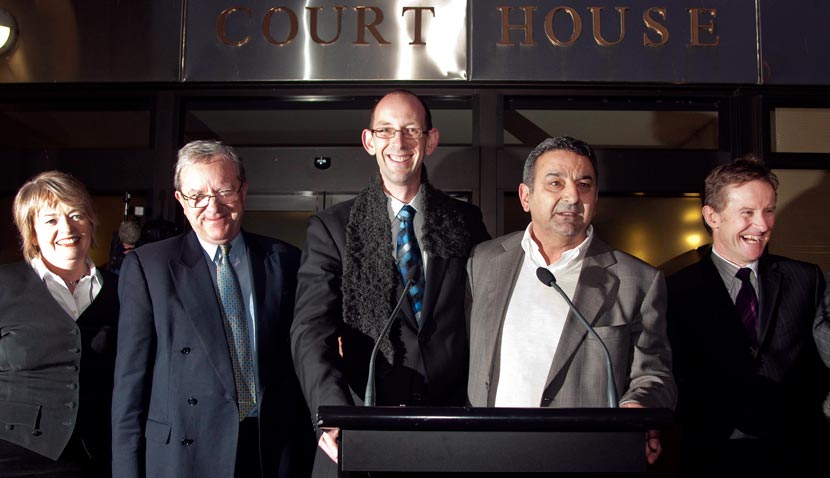 Group of smiling people in suits standing behind a lectern and microphone