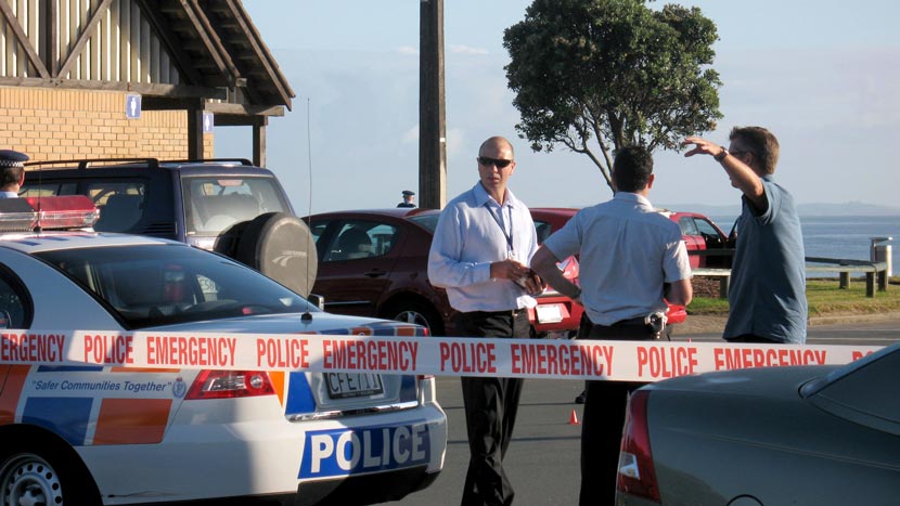 Three men talking next to police car and behind Police Emergency crime scene tape