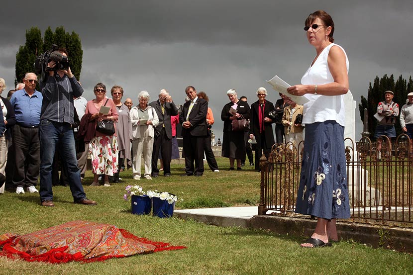 Group of people gathered in a cemetery beside covered headstone on overcast day