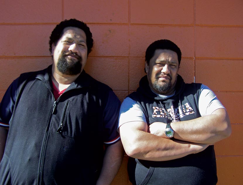 Two men stand against a wall.