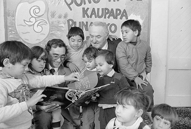 Young children read a picture book with two men.