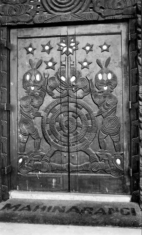 Elaborately carved wooden doorway with a mat inscribed with the word Mahinarangi on the ground in front of the door.