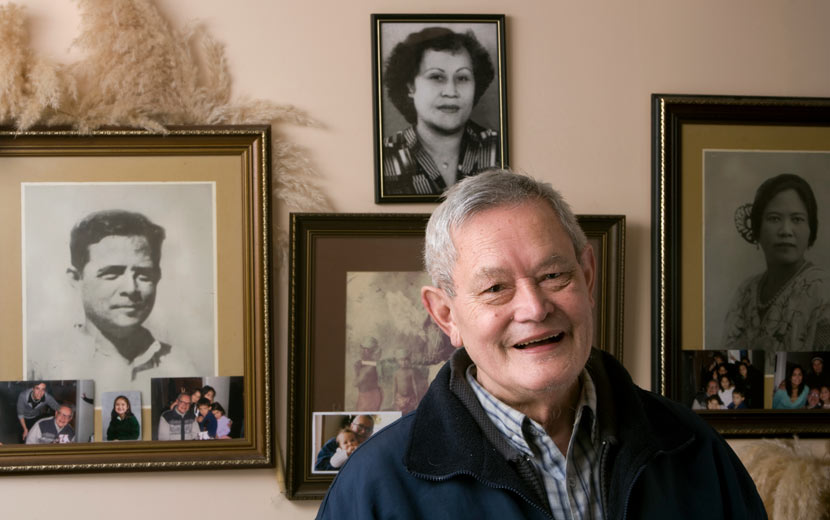 A photograph of Joseph Churchward standing in front of a wall hung with framed photographs