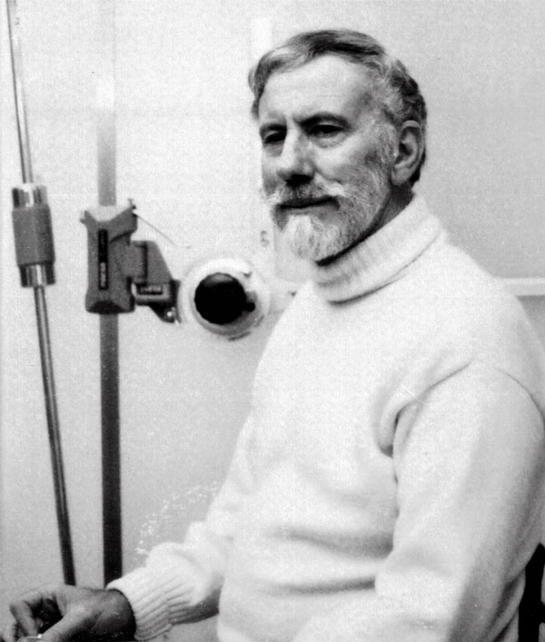Man in white jersey sitting beside a architectural drawing board.