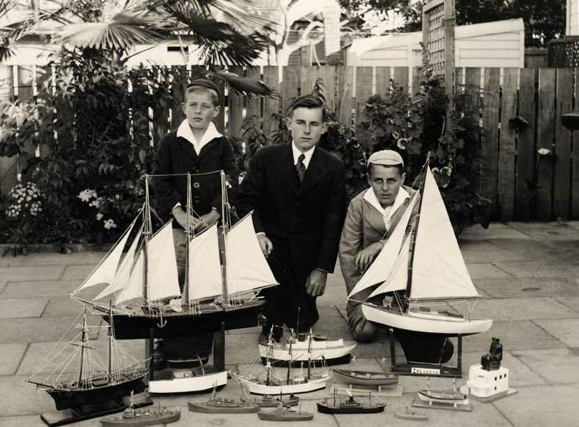 A photograph showing three boys posed behind 15 model ships