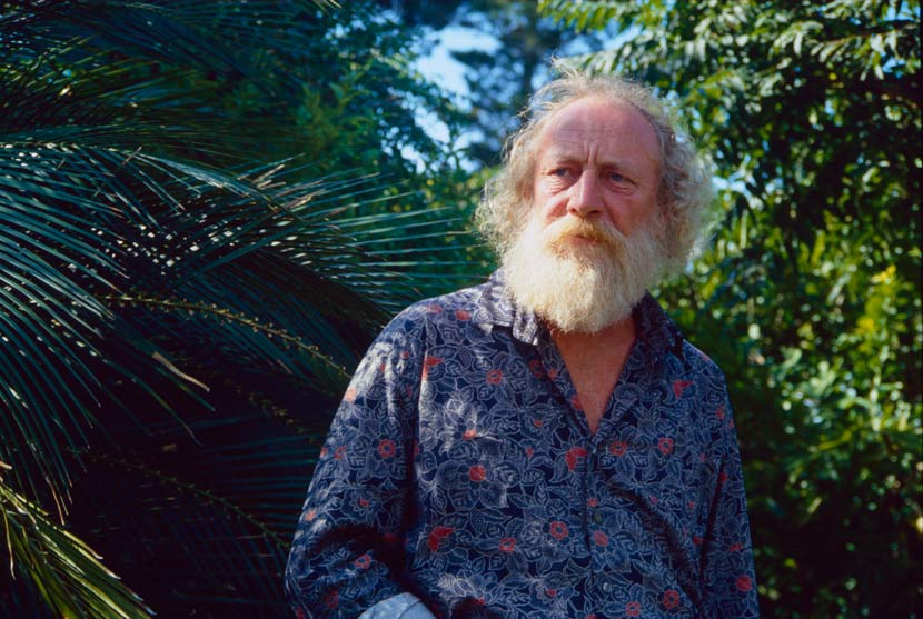 A photograph of a bearded Ted Smyth standing outdoors with vegetation behind him