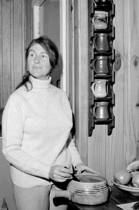 Peggy Laird in middle age, posing with a rack of pottery cups and a pottery serving dish. 