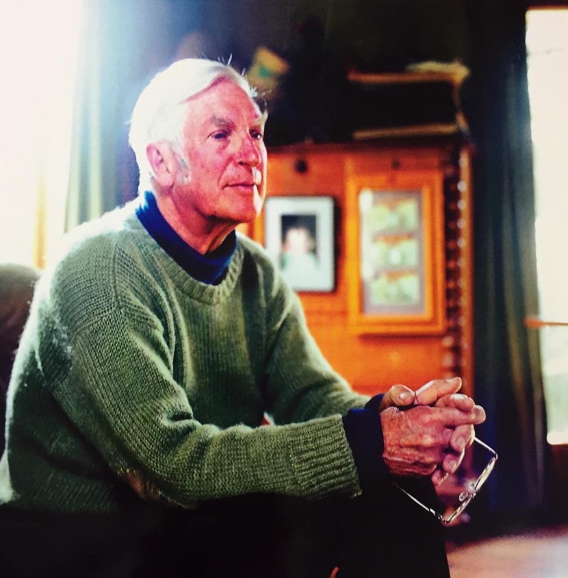 Harry Turbott, seated and holding his glasses in his hand.