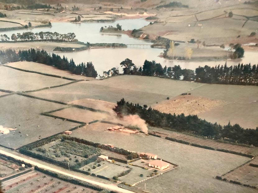 A colour aerial photograph showing flat farmland beside a river, lined with trees, hedges, cultivations and roads. There are low hills in the distance.