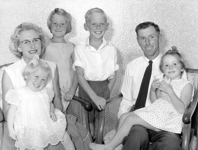 A black and white formal portrait showing Roly and Irene Earp and their family, well-groomed and tidily dressed. The adults, in their thirties, are seated in wicker chairs, each with a young child on their laps, with two older children standing between them. 