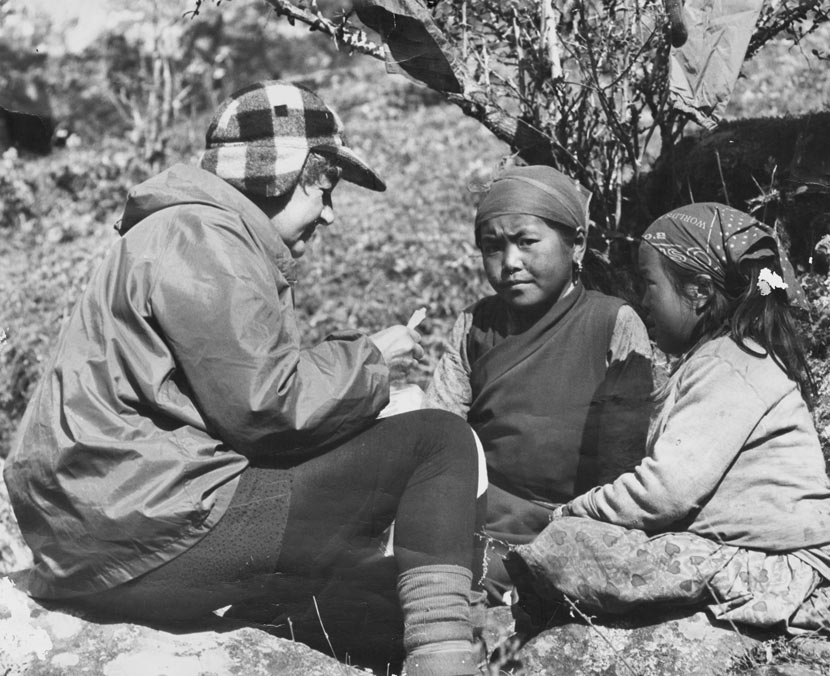 Mavis Davidson seated on the ground in profile, with two Tibetan children. 