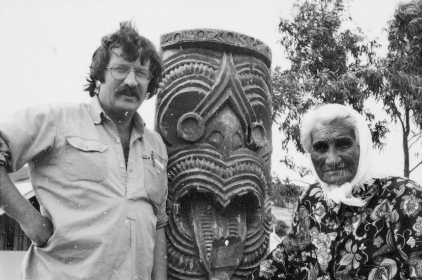 Michael King and Whina Cooper, standing either side of a carved pou (pole). 