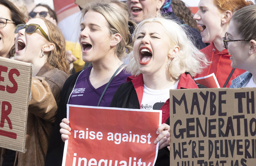 Women standing in tight group, holding protest signs and shouting.