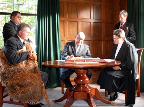 Five people gathered around a wooden desk signing papers.