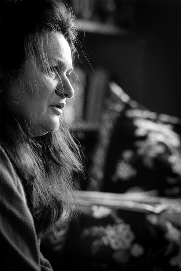 Photo of a woman with long dark hair, standing in profile, looking to the right of the frame, as if in mid-sentence. 