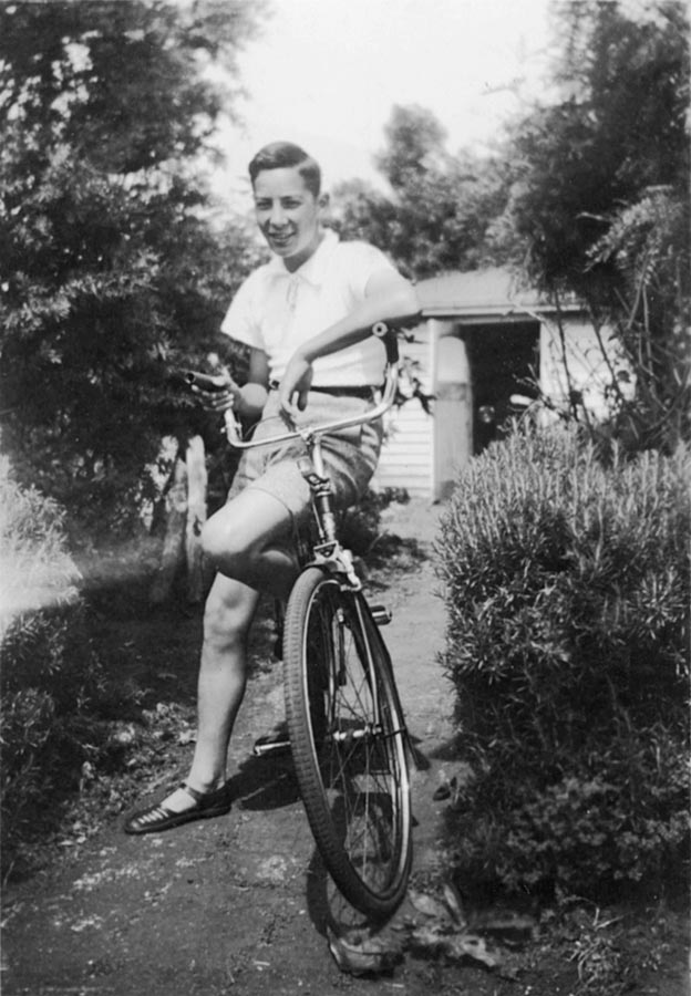 Hugh Kawharu, aged about 12, seated on a bicycle in the garden at his home.