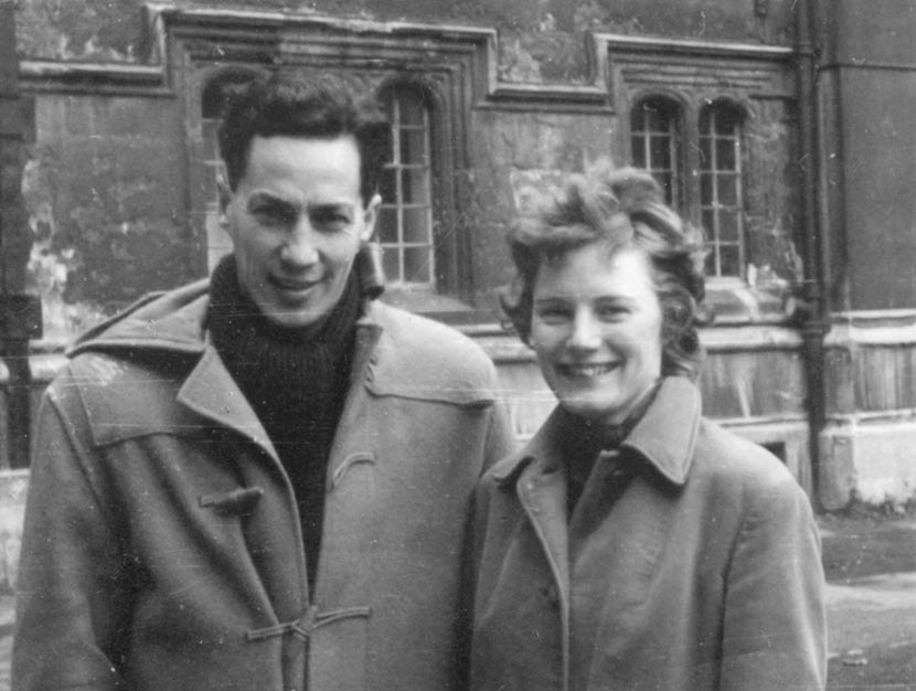 A smiling young couple stand side by side in heavy winter coats.