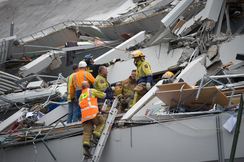 People in emergency uniforms gathered on the remains of a crushed building.