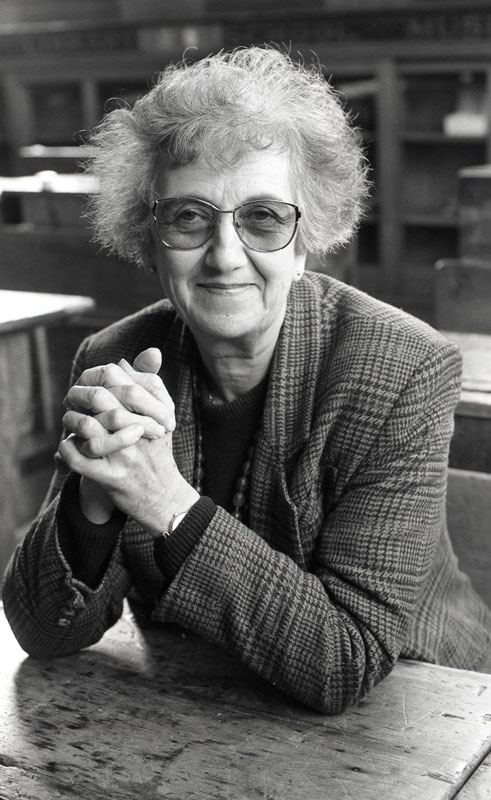 A photograph of Mina McKenzie, in middle age, seated at a table.